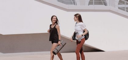 Two women in active wear walking outdoors while smiling and carrying yoga mats.