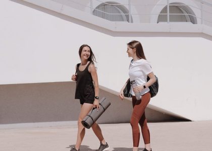 Two women in active wear walking outdoors while smiling and carrying yoga mats.