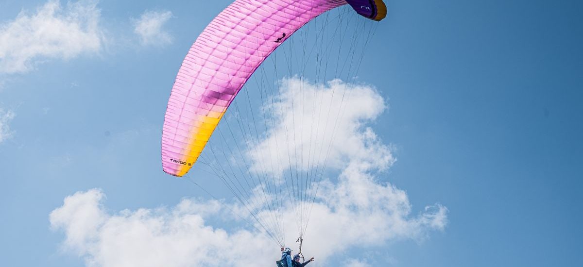 Experience the thrill of tandem paragliding with colorful parachute soaring high in the clear blue sky.