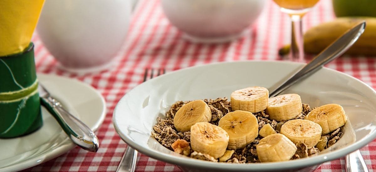 A healthy breakfast bowl with sliced bananas and cereal on a red checkered tablecloth.