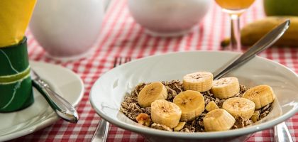 A healthy breakfast bowl with sliced bananas and cereal on a red checkered tablecloth.