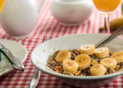 A healthy breakfast bowl with sliced bananas and cereal on a red checkered tablecloth.