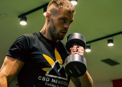 Muscular man exercising with a dumbbell in a modern gym setting, emphasizing strength and fitness.